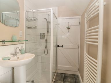 A bathroom with a shower enclosure sink with mirror and towel radiator at Glasfryn in Llanfaethlu
