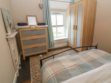 A bedroom with a bed, wooden wardrobe, chest of drawers with towels, window, and a small fireplace at Glasfryn in Llanfaethlu