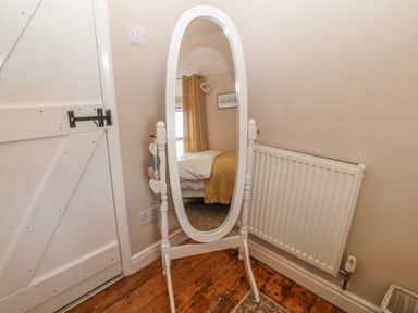 A full length mirror on a stand next to a radiator and a wooden door at Glasfryn in Llanfaethlu