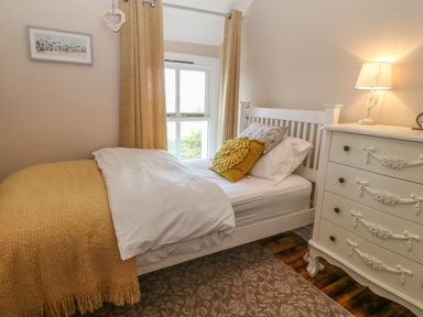A bedroom with a single bed yellow curtains a white dresser with a lamp and a window at Glasfryn in Llanfaethlu