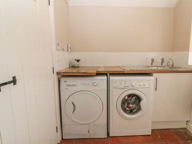 A utility room with a washing machine and dryer under a wooden countertop with a sink at Glasfryn in Llanfaethlu