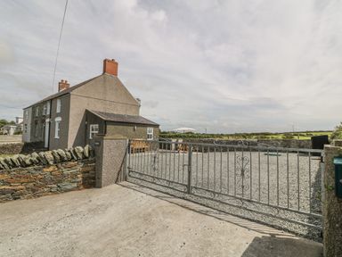 A two-story house with brick chimneys surrounded by a stone wall and metal gate at Glasfryn in Llanfaethlu