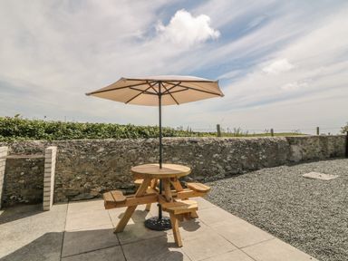 A wooden picnic table with an umbrella on a stone patio near a stone wall at Glasfryn in Llanfaethlu