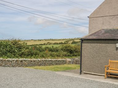 An outdoor area with a gravel driveway wooden bench stone wall and green fields in the background at Glasfryn in Llanfaethlu