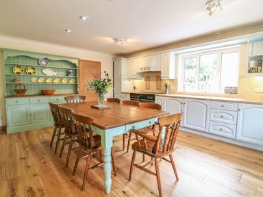 A kitchen with a wooden dining table surrounded by chairs and cabinets along the wall at Wood View Cottage in Blackawton