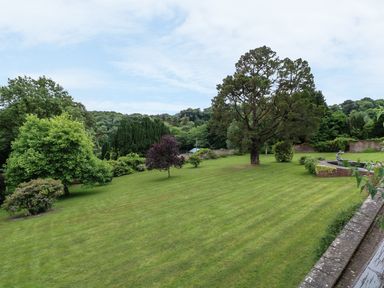 A large lawn with trees and a stone pond with a statue in a garden at Wood View Cottage in Blackawton