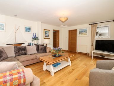 A living room with a sofa, armchair, wooden coffee table, TV on a stand, paintings on the walls and wooden doors at Wood View Cottage in Blackawton
