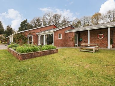 A brick house with a garden bed and a wooden picnic table on grass at Wood View Cottage in Blackawton