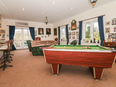 A game room with a pool table green leather chairs bar stools and windows with blue curtains at Wood View Cottage in Blackawton