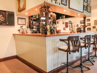 An indoor bar area with stools dartboard and framed pictures at Wood View Cottage in Blackawton