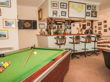 A game room with a pool table a dartboard and a bar with stools at Wood View Cottage in Blackawton