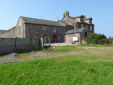 Stone and brick buildings with a wooden fence and grassy area at Muncaster View in Carleton near Ravenglass