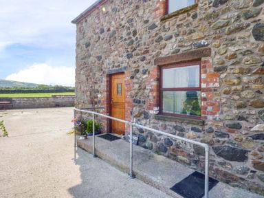 Stone exterior wall with a wooden door and window with metal railing on concrete steps at Muncaster View in Carleton near Ravenglass