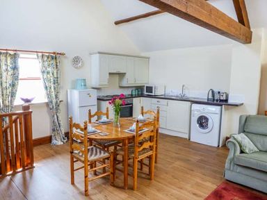 A kitchen and dining area with wooden table and chairs washing machine and green armchair at Muncaster View in Carleton near Ravenglass