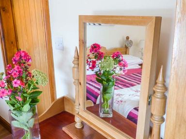 A wooden dressing table with a mirror and a glass vase with pink and white flowers at Muncaster View in Carleton near Ravenglass
