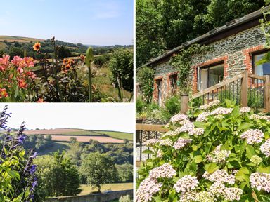 A garden with flowers and greenery outside a stone cottage with wooden railing at Rose Cottage in Barnstaple
