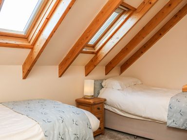 A bedroom with two single beds a wooden bedside table and skylight windows in the ceiling at Rose Cottage in Barnstaple