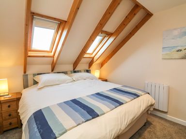A bedroom with a double bed two bedside tables with lamps skylight windows and a painting on the wall at Rose Cottage in Barnstaple