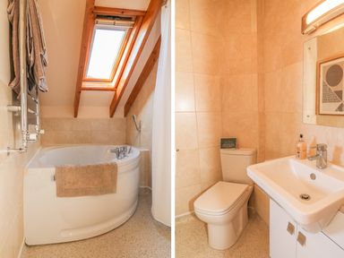 A bathroom with a corner bathtub under a skylight and a separate area with a toilet and a sink with a mirror at Rose Cottage in Barnstaple