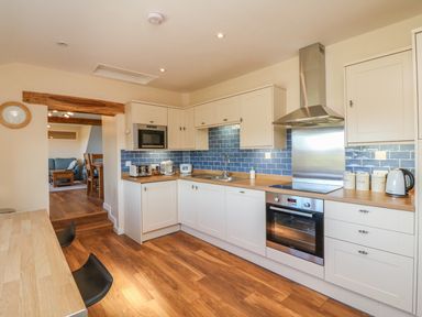 A kitchen with white cabinets blue tiled backsplash and wooden counters next to a dining area at Rose Cottage in Barnstaple
