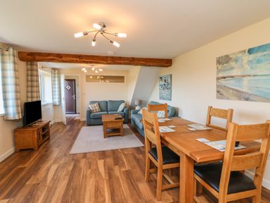 A living room with a wooden dining table and chairs two sofas a coffee table a TV on a stand and wall paintings at Rose Cottage in Barnstaple