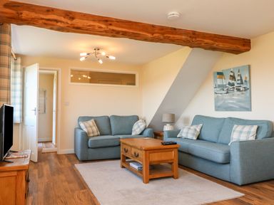 A living room with two blue sofas a wooden coffee table a television and wall art at Rose Cottage in Barnstaple