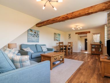 A living room with blue sofas wooden tables a dining table paintings and a bookshelf at Rose Cottage in Barnstaple