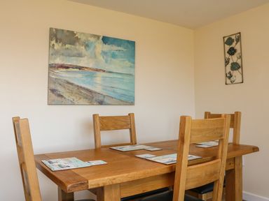 A dining room with wooden table and chairs and a seascape painting on the wall at Rose Cottage in Barnstaple