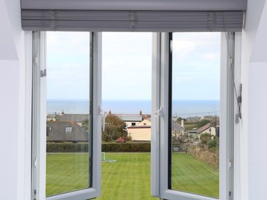 A view from an open window overlooking a lawn garden houses and the sea at Myles View in Pendeen