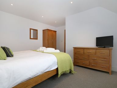 A bedroom with a bed covered in white sheets and green blanket a wooden wardrobe a wooden dresser with a television and a wall mirror at Myles View in Pendeen