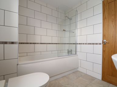 A bathroom with a bathtub shower and wood door at Myles View in Pendeen