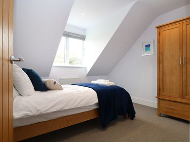 A bedroom with a bed with pillows and folded towels a wooden wardrobe and a window at Myles View in Pendeen