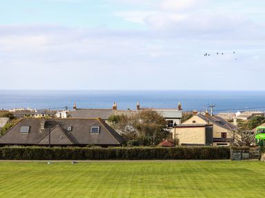 A view of houses and the ocean beyond a grassy field at Myles View in Pendeen