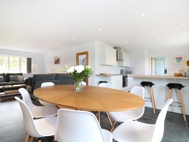A dining area with a wooden oval table and white chairs with a vase of flowers in a kitchen and living room at Myles View in Pendeen