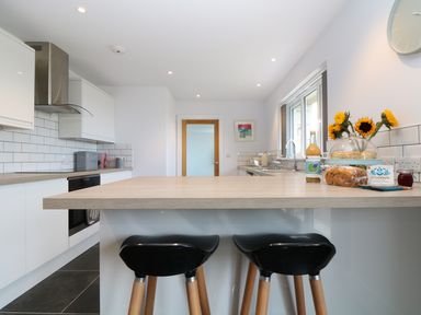 A kitchen with two black stools at a wooden island and sunflower bouquet at Myles View in Pendeen