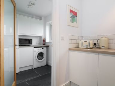 A kitchen area with a toaster and kettle on the counter and an adjacent utility room with a washing machine microwave and fire extinguisher at Myles View in Pendeen