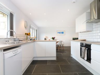 A kitchen with white cabinets a stainless steel oven and a dining table with chairs at Myles View in Pendeen