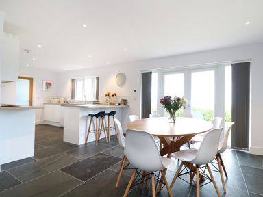 A kitchen and dining area with a round wooden table and white chairs at Myles View in Pendeen
