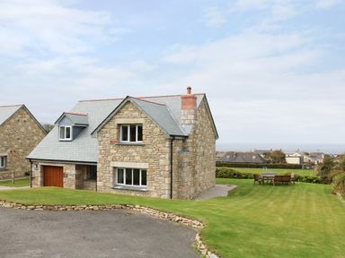 A stone house with a garage and a lawn with outdoor furniture at Myles View in Pendeen