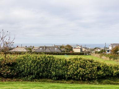A grassy field with a hedge in front and houses in the distance at Myles View in Pendeen