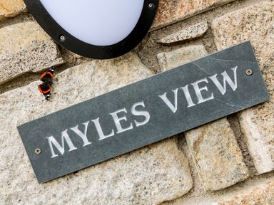 A stone wall with a black plaque that reads Myles View and a butterfly near a black and white wall light at Myles View in Pendeen