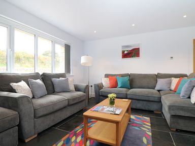 A living room with grey sofas and a wooden coffee table on a colorful rug at Myles View in Pendeen