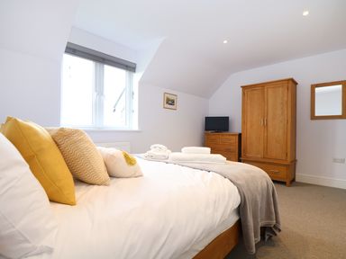 A bedroom with a bed with yellow pillows and folded towels a wooden wardrobe and chest of drawers with a television at Myles View in Pendeen