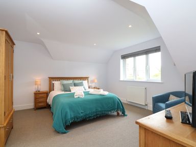 A bedroom with a wooden bed with teal bedding next to wooden bedside tables and a wardrobe with a window and a blue armchair at Myles View in Pendeen