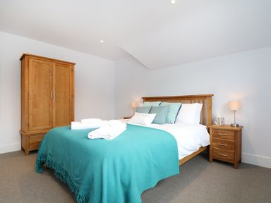 A bedroom with a wooden bed with blue blankets two bedside tables with lamps and a wooden wardrobe at Myles View in Pendeen