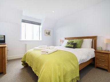 A bedroom with a double bed green blanket and pillows a wooden dresser and nightstand by the window at Myles View in Pendeen