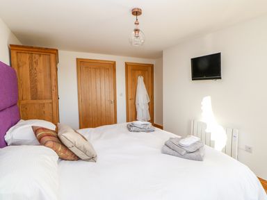 A bedroom with a bed made with white linens, folded towels on the bed, wooden doors, a wooden wardrobe, and a wall-mounted television at Apple Tree Cottage in Bleatarn near Kirkby Stephen