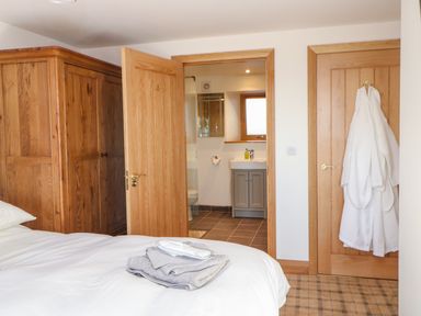 A bedroom with a bed and wooden wardrobe showing an open door to a bathroom at Apple Tree Cottage in Bleatarn near Kirkby Stephen