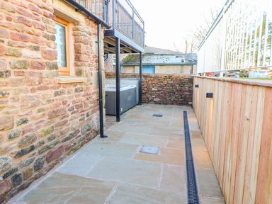 An outdoor patio area with stone walls a wooden fence a window and a hot tub at Apple Tree Cottage Bleatarn near Kirkby Stephen