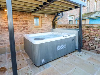 An outdoor hot tub under a wooden deck beside a stone wall at Apple Tree Cottage in Bleatarn near Kirkby Stephen